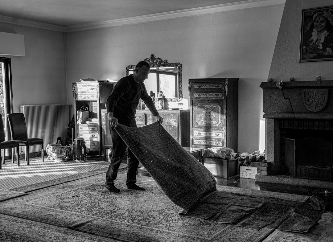 a-black-and-white-photo-of-a-man-moving-a-rug-p70tanqhfeo
